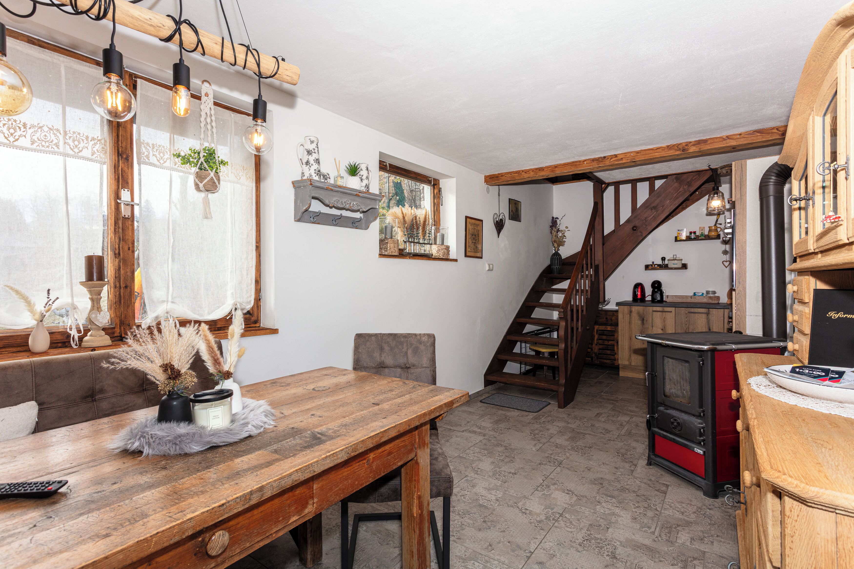 A cozy kitchen with a wooden table, hanging light bulbs, and a red stove.