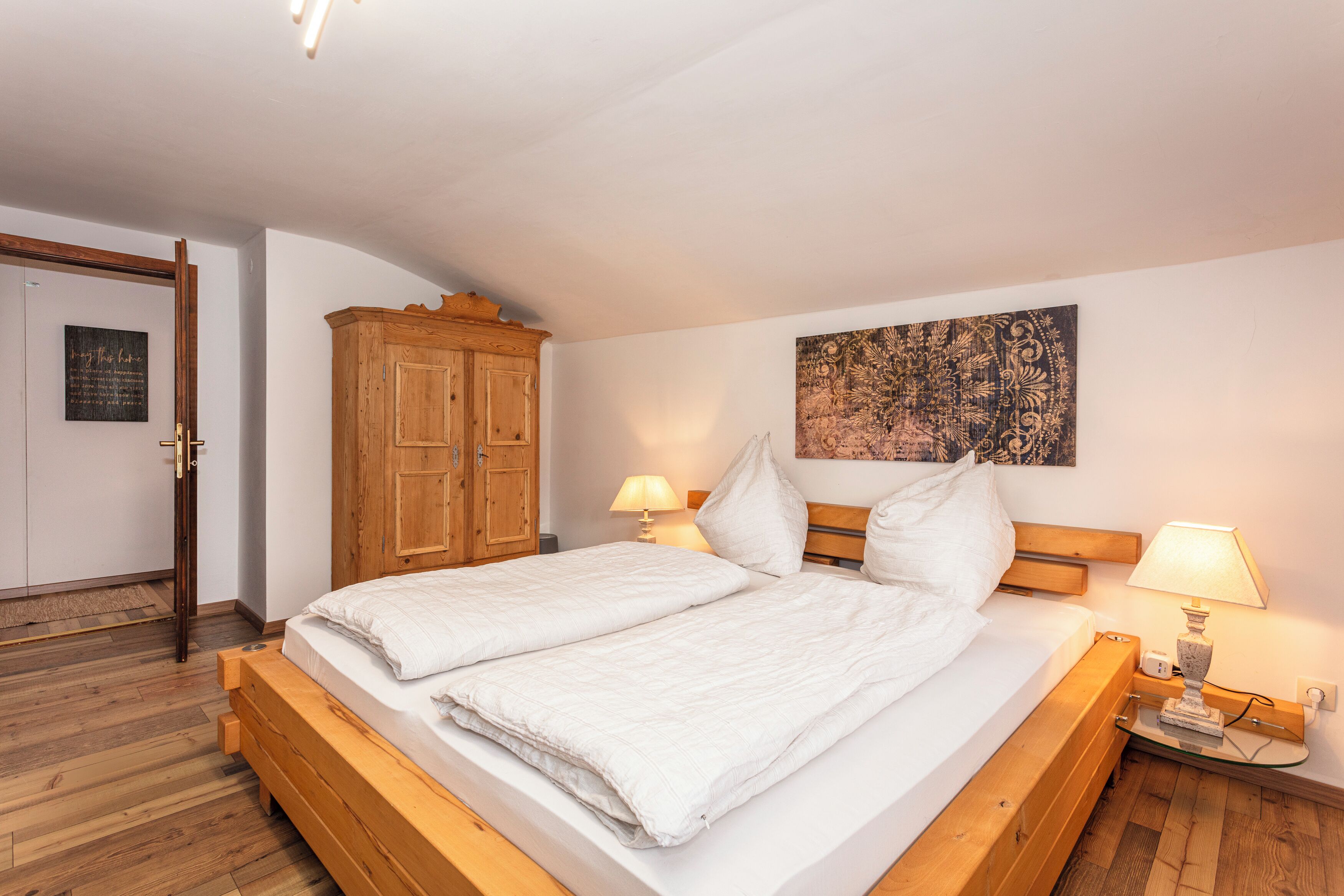 Un dormitorio con una cama de madera, dos lámparas de noche, un armario de madera y un tapiz colgado en la pared.