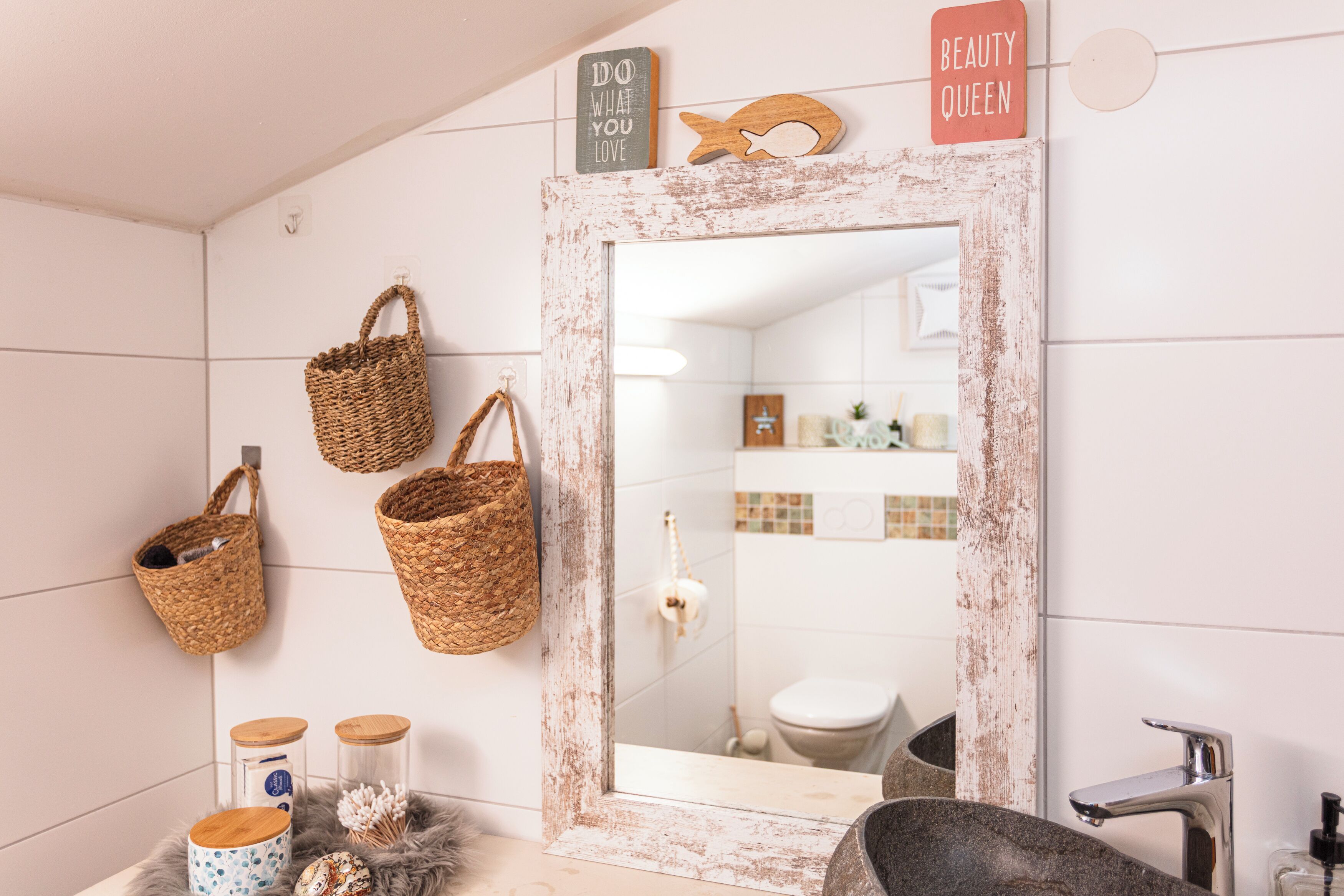 A bathroom with a rustic mirror, wicker baskets, and a 'Beauty Queen' sign.