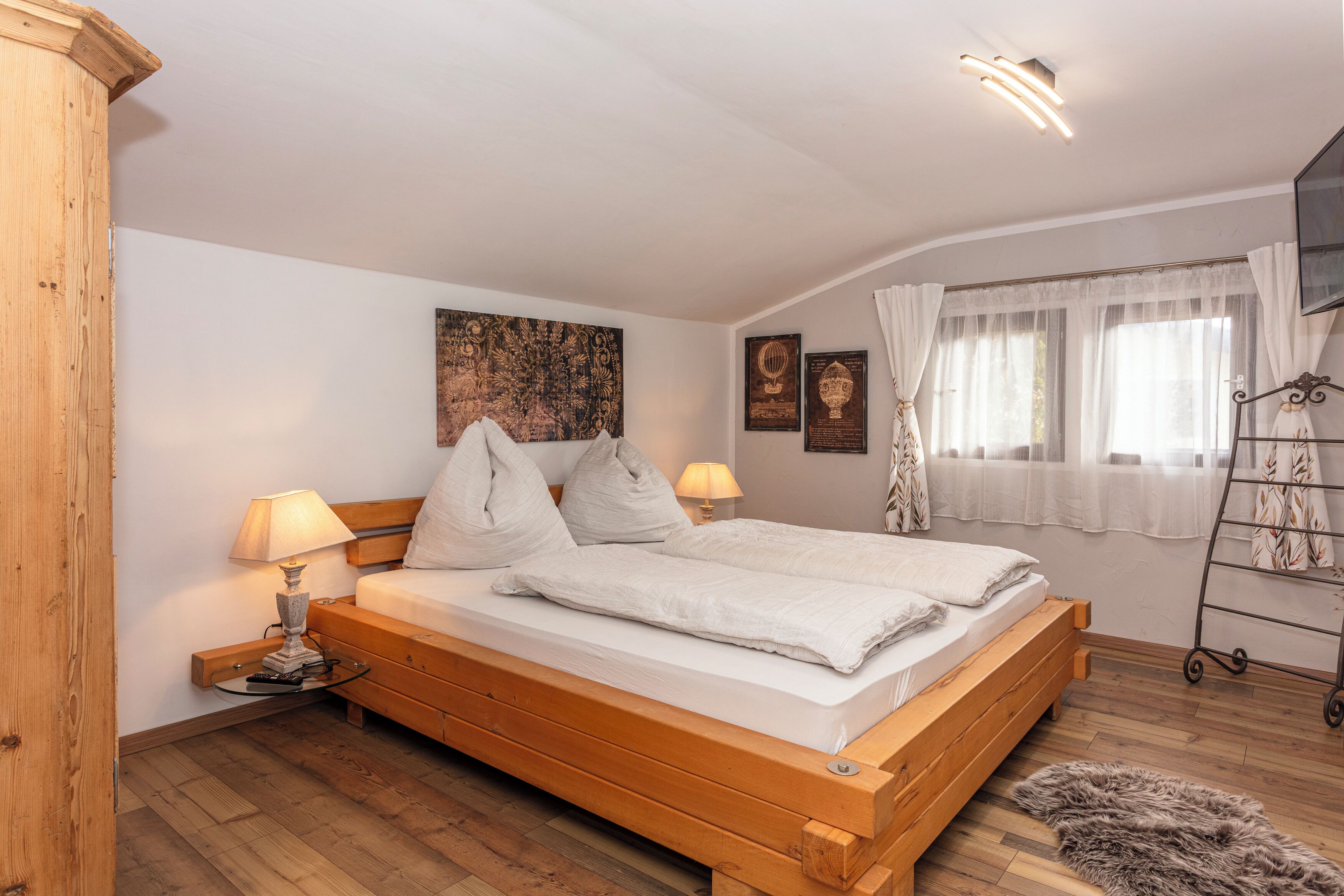 Ein Schlafzimmer mit einem hölzernen Bett, zwei Nachttischen mit Lampen, einer großen Wandteppich und einem Fenster mit Vorhängen.