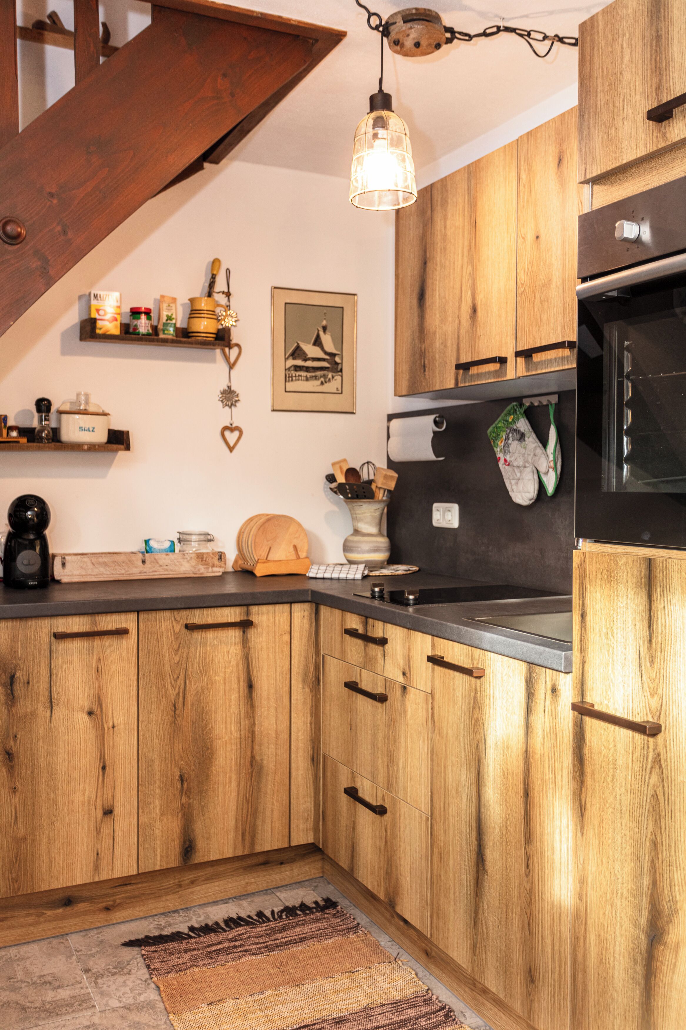 Een keuken met houten kasten, een zwarte magnetron en een hanglamp.