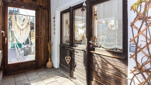 Une porte en bois avec une poignée en forme de cœur, une fenêtre ornée d’une cloche et une structure en treillis sur le côté droit.