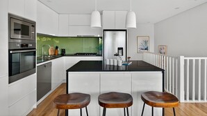 Une cuisine moderne avec des meubles blancs, un plan de travail noir et trois tabourets en bois.