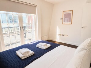 A hotel room with a bed, a window with blinds, a wall-mounted artwork, and a door. - 2BR Penthouse with balcony (Greater London)