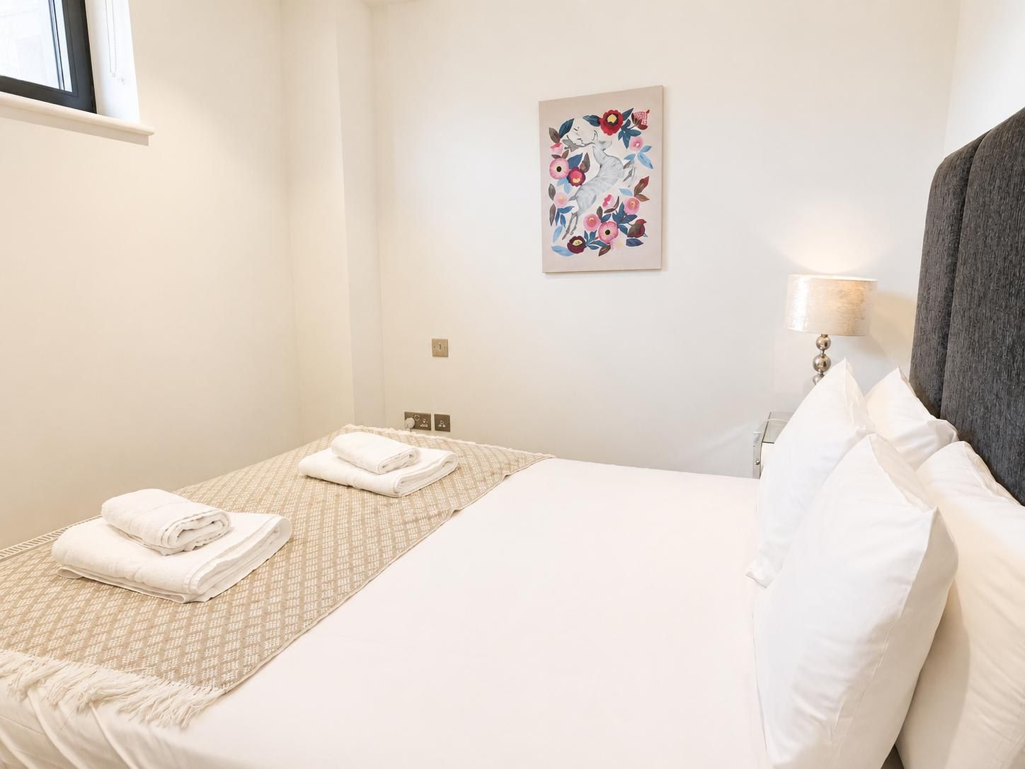 A hotel room with two beds, a window, a wall-mounted artwork, and a bedside lamp.