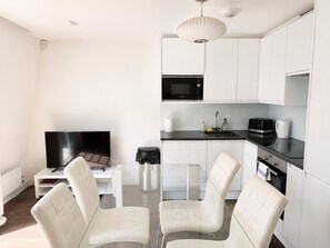 A modern kitchen with white cabinets, a black microwave, and a coffee maker. - 2BR Penthouse with balcony (Greater London)