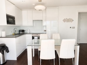 A modern kitchen with white cabinetry, a stainless steel microwave, and a glass dining table with white chairs. - 2BR Penthouse with balcony (Greater London)