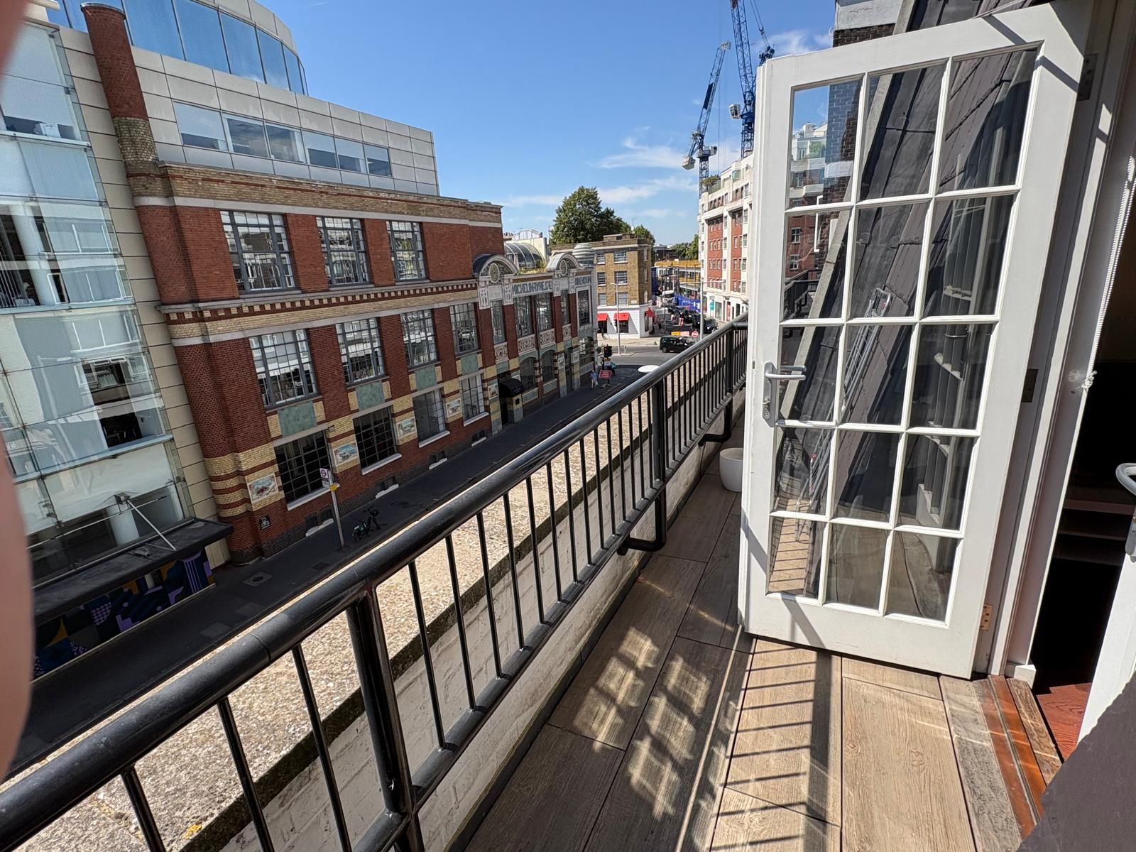 A balcony with a metal railing overlooking a street with buildings, including a red brick building and a modern glass structure.