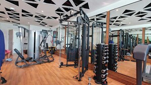 A gym with various exercise equipment, wooden flooring, and a modern ceiling design. - StayShort - Comfortable Studio Stay in Square Tower Ideal for 2 (JVC)