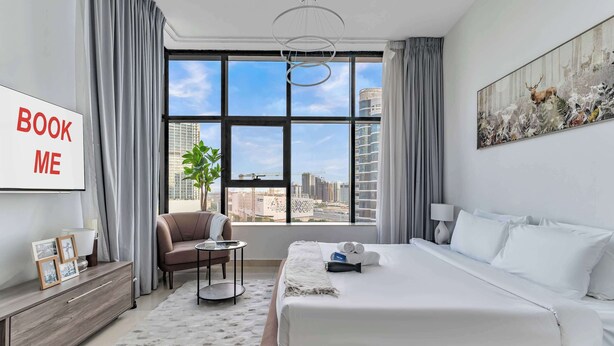 A modern hotel room with a large bed, a desk, a chair, and a view of the city. - StayShort - Comfortable Studio Stay in Square Tower Ideal for 2 (JVC)