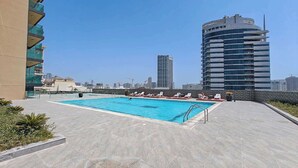 A rooftop pool with lounge chairs and a city skyline in the background. - StayShort - Comfortable Studio Stay in Square Tower Ideal for 2 (JVC)