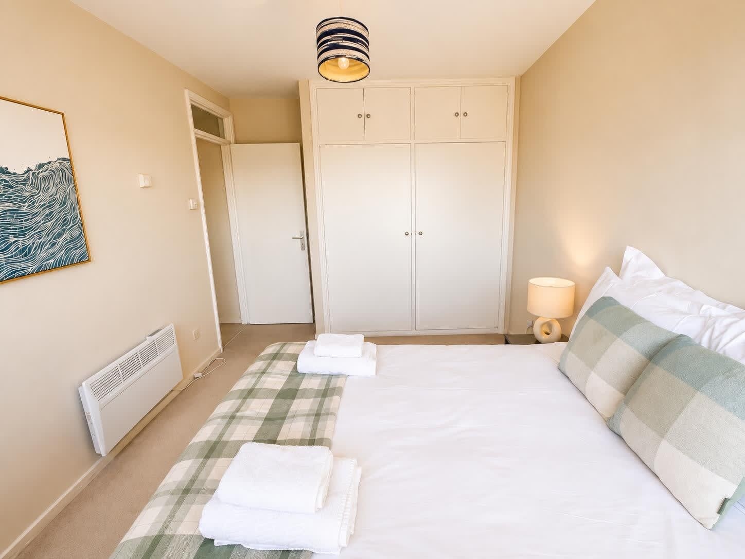 Une chambre d’hôtel comprenant un lit, une armoire, un radiateur, une œuvre d’art accrochée au mur et une lampe de chevet.