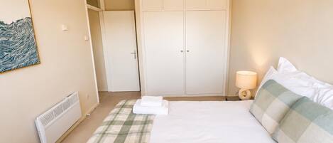 Une chambre d’hôtel comprenant un lit, une armoire, un radiateur, une œuvre d’art accrochée au mur et une lampe de chevet.