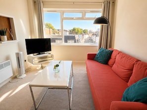 Ein Wohnzimmer mit einer Couch, einem Couchtisch, einem Fernseher und einem Fenster mit Vorhängen.