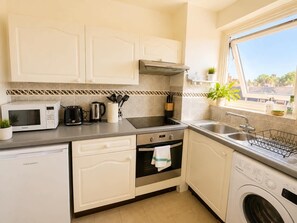 A compact kitchen with a microwave, toaster, kettle, and a washing machine. - The Elden - No.15 (Greater London)