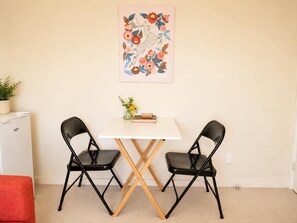 Ein Zimmer mit einem weißen Tisch, zwei schwarzen Stühlen, einer kleinen Pflanze und einem gerahmten Bild an der Wand.