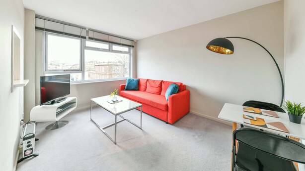 A modern living room with a red sofa, a white coffee table, a flat-screen TV, and a black floor lamp. - The Elden - No.15 (Greater London)