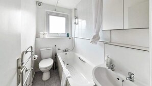 A modern bathroom with a toilet, bathtub, and sink. - The Elden - No.15 (Greater London)