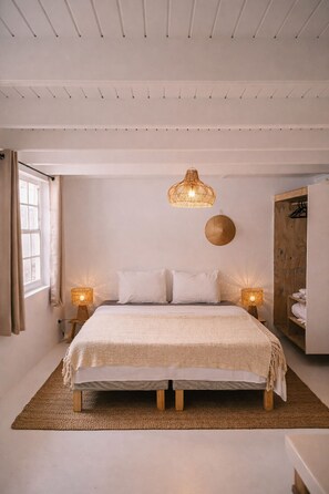 A bedroom with a bed, two bedside lamps, a hanging light fixture, a round wall decoration, and a wooden wardrobe. - Deluxe - 4 Person - Apartment (Willemstad)