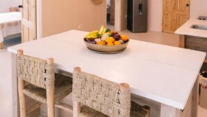 Eine moderne Küche mit einer großen Kochinsel, Korbstühlen, einer Obstschale und einer Holztür.