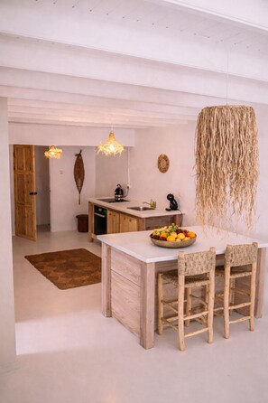 A kitchen with a central island, wooden chairs, a fruit bowl, and hanging light fixtures. - Deluxe - 4 Person - Apartment (Willemstad)