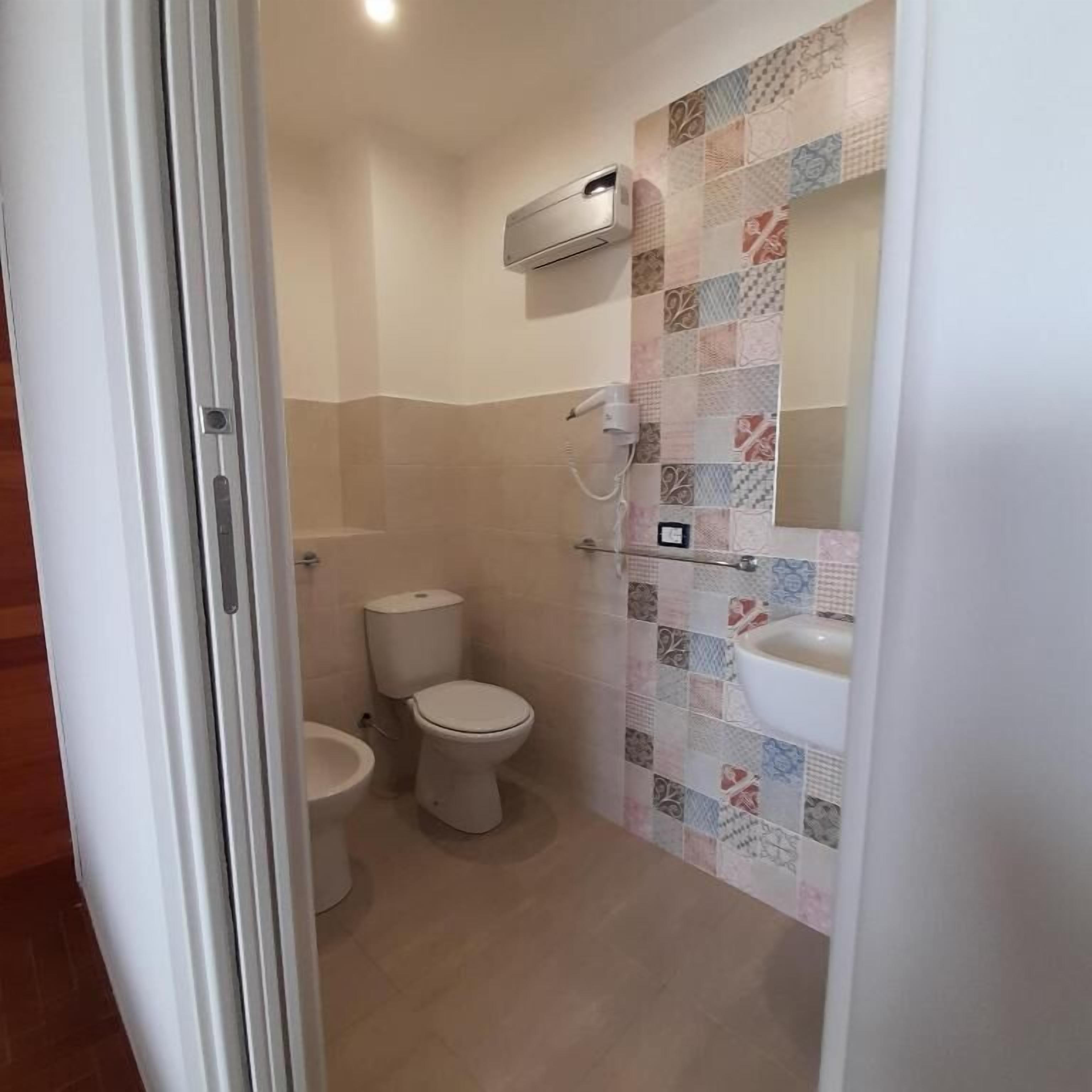 A bathroom with a toilet, bidet, and a wall-mounted air conditioner.