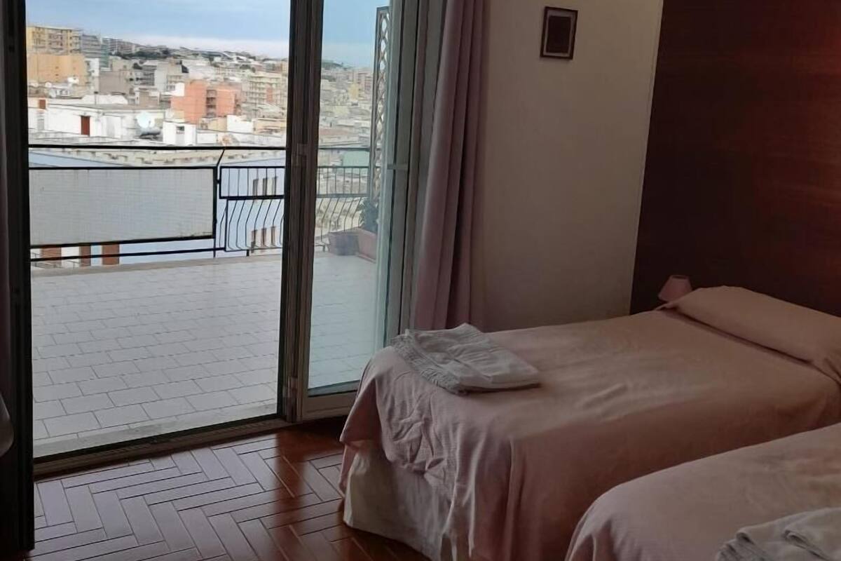 Hotellihuone, jossa on parveke, sänky ja näkymä kaupunkiin.