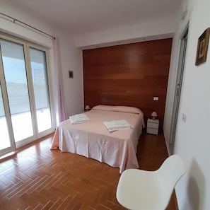 Camera da letto con testiera in legno, letto con lenzuola bianche, comodino con lampada e una poltrona.