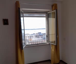A room with a window, yellow curtains, and a view of a body of water and buildings.