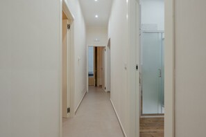 Un corridoio stretto con pareti bianche e pavimento in legno, che conduce a una stanza con una porta in vetro.