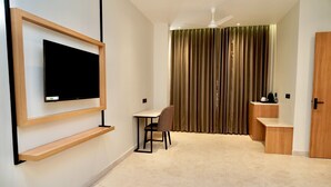 Quarto de hotel moderno com televisão de tela plana na parede, uma mesa pequena com uma cadeira, uma escrivaninha com cadeira, ventilador de teto e porta de correr com cortinas.