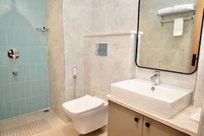 A bathroom with a white toilet, a sink with a mirror above it, and a shower area with a glass door. - Hotel HBP Grand (Bhadohi)