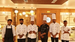 Um grupo de chefs em uma cozinha com painéis de madeira e luminárias modernas.