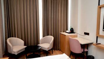 Habitación de hotel con dos sillones, una pequeña mesa redonda, un escritorio con silla, una cama y un minibar.