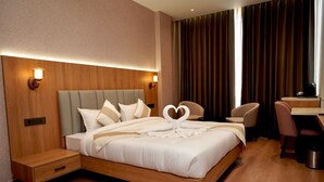 Quarto de hotel com uma cama grande, duas mesas de cabeceira, uma escrivaninha e uma cadeira.