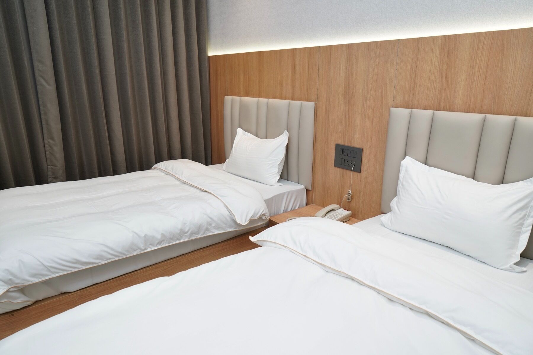 A hotel room with two beds, a wooden headboard, and a telephone on the nightstand.