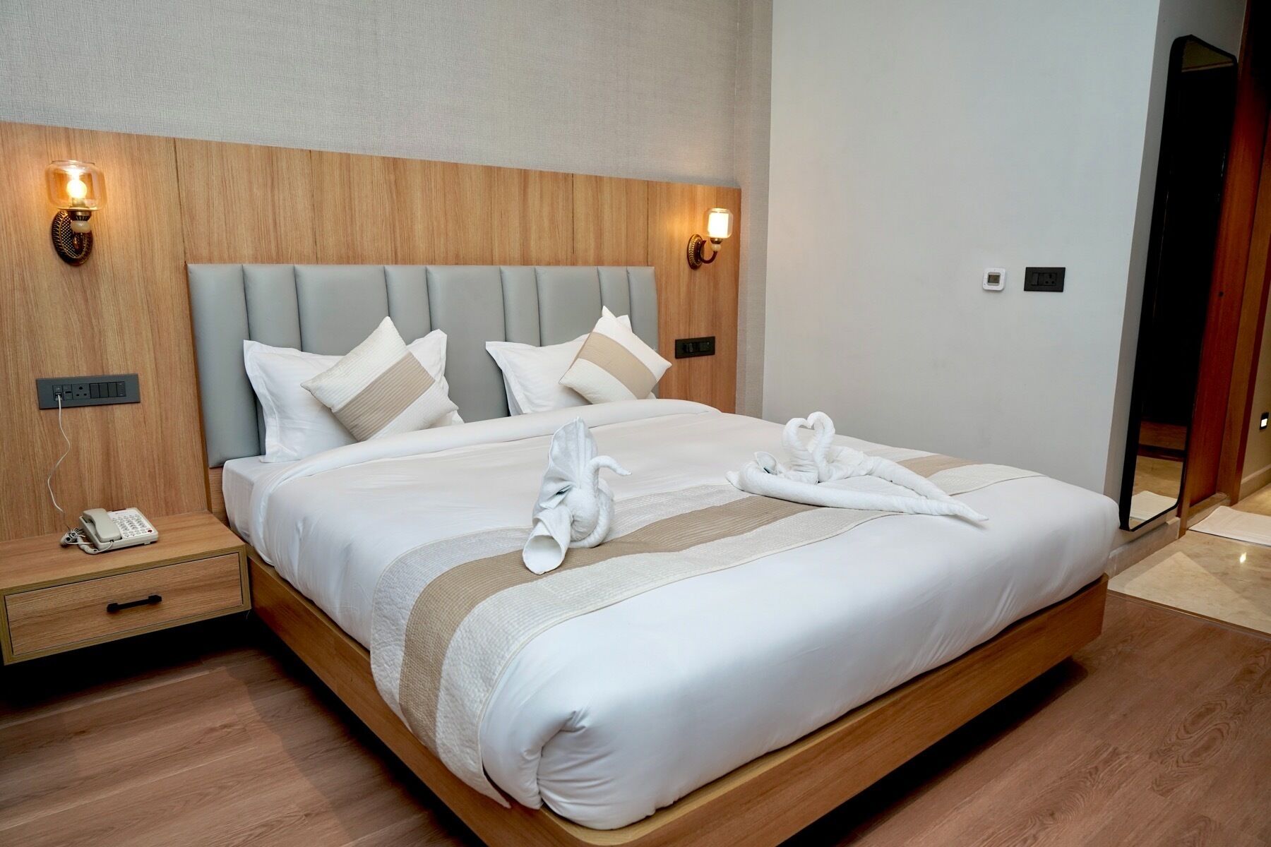 A neatly made bed with white linens, two bedside lamps, a phone on the nightstand, and a wooden headboard.