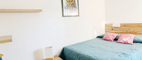 A bedroom with a bed, a chair, a bedside table, a framed picture on the wall, and a wooden headboard.