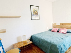 Un dormitorio con cama, una silla, una mesita de noche, un cuadro enmarcado en la pared y un cabecero de madera.