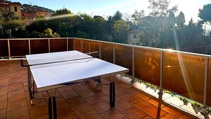 Un tavolo da ping pong su un balcone con vista su alberi e palazzi.