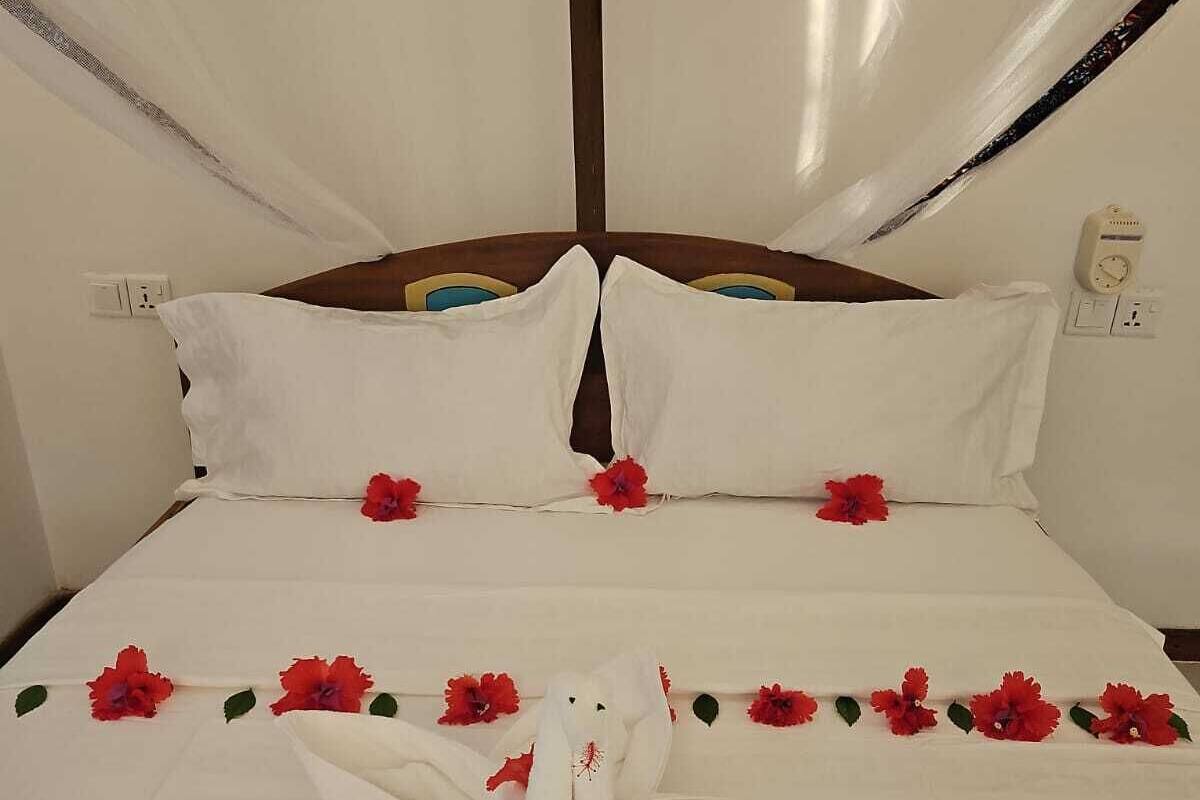 Un lit avec du linge de lit blanc, des fleurs rouges et une sculpture faite avec une serviette.