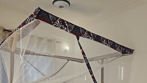Un letto a baldacchino, lenzuola bianche e fiori rossi.
