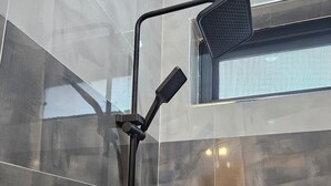 Doccia con soffione a mano e soffione fisso, montata su una parete con piastrelle scure.