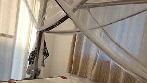 Un letto con lenzuola bianche, un baldacchino e petali di fiori rossi.