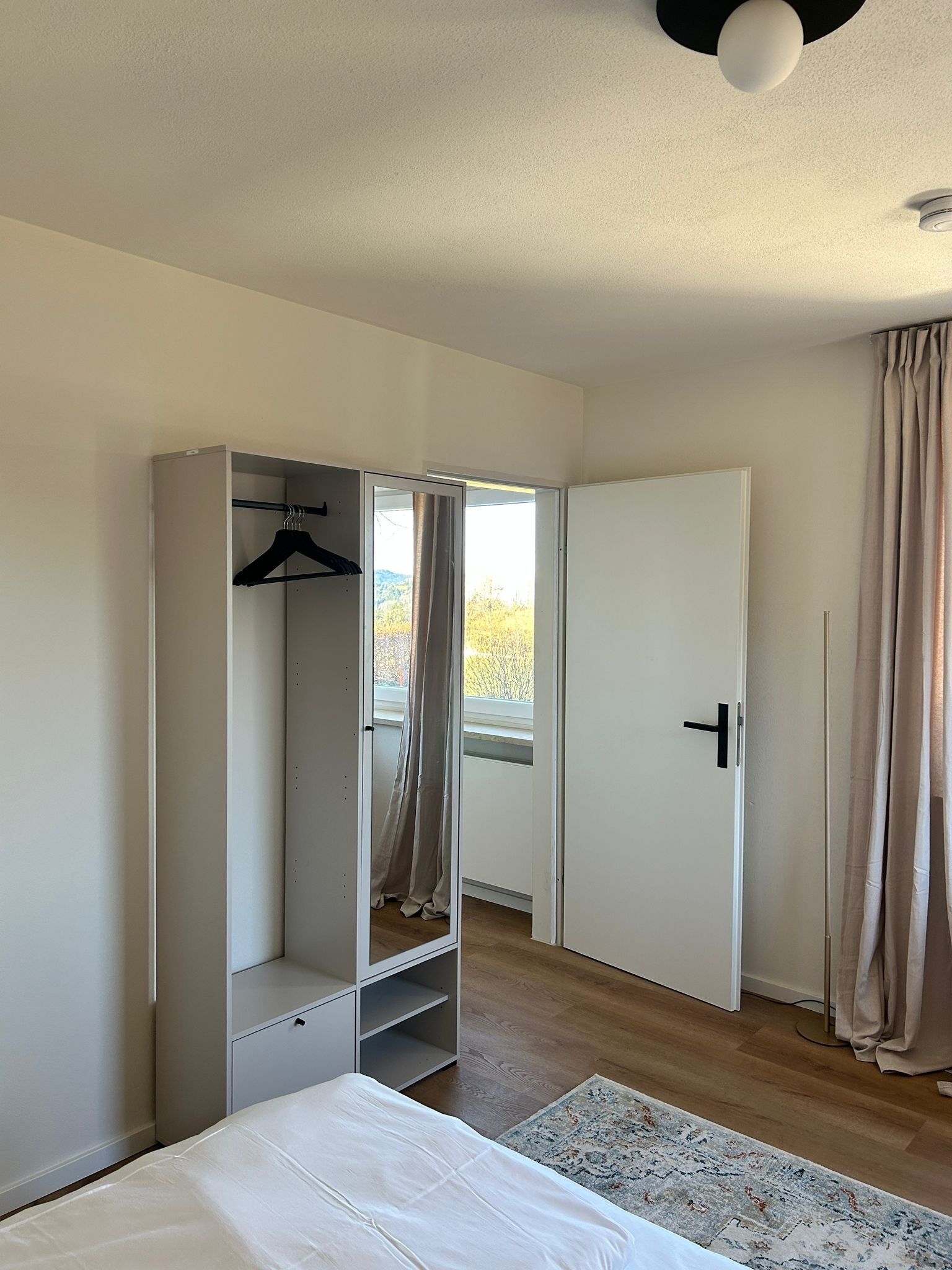 A bedroom with a bed, a wardrobe, a door, and a window with curtains.