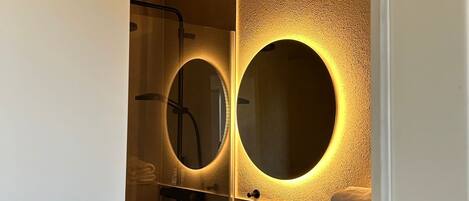 Une salle de bain moderne avec un grand miroir, un lavabo rond et une douche.