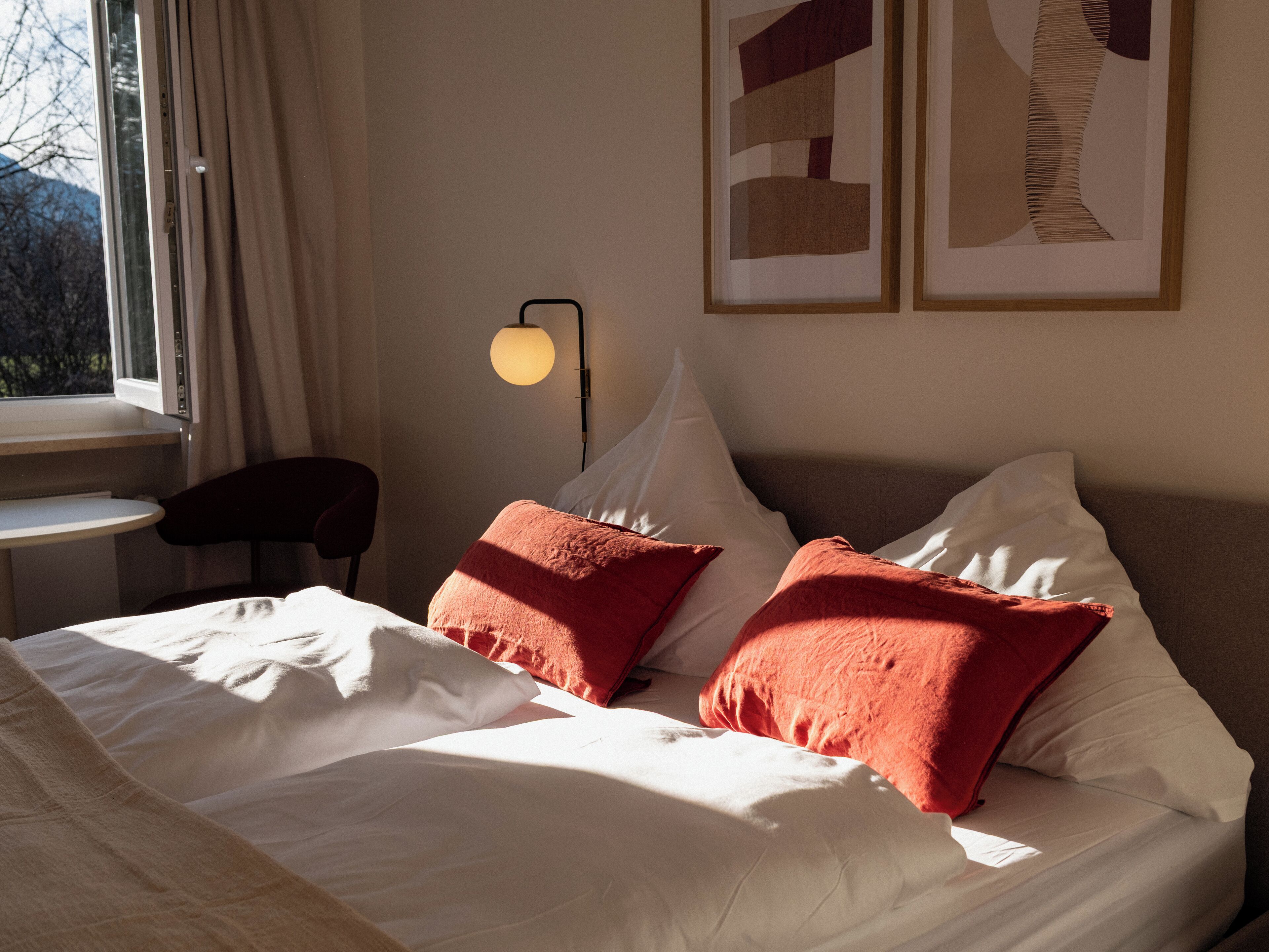 A hotel room with a bed, a desk, a chair, and a lamp.