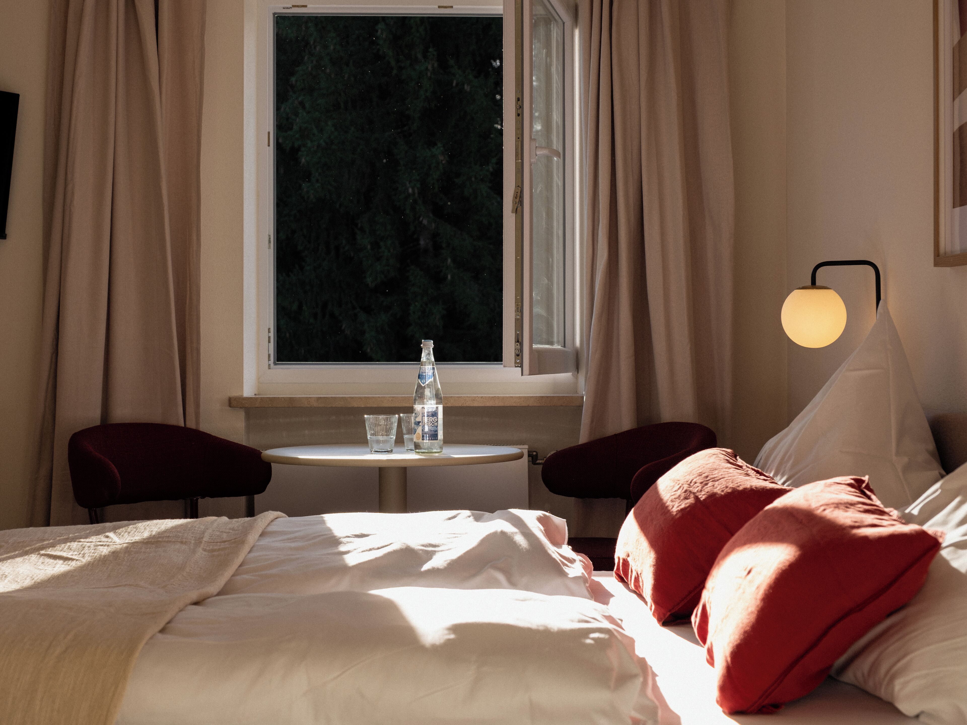 Habitación de hotel con cama, dos sillas, una mesita, una botella y vasos.