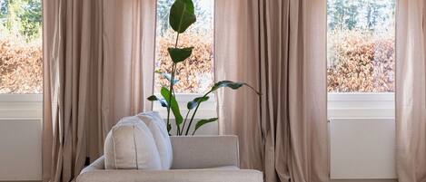 A modern living room with a beige sofa, two white side tables, and a large window with beige curtains.