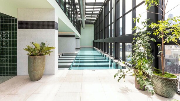 Un espacio interior moderno con una escalera de cristal, plantas en macetas y vistas a la ciudad.